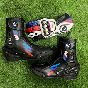 Puede incluir: Un par de botas de moto negras y un guante de moto a juego. Las botas presentan el logotipo de BMW, detalles en azul y rojo y placas protectoras de pl&aacute;stico. El guante es blanco, negro, rojo y azul con un protector met&aacute;lico para los nudillos.