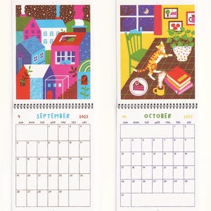 May include: A 2027 wall calendar showing September and October pages. September features a colorful town illustration, while October depicts a cat on a table with a cake and coffee. Each page includes a grid with days of the week and dates.