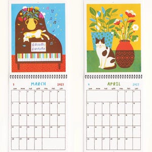 May include: A wall calendar showing March and April 2027. The March page features a brown piano with a cat, a vase of flowers, and musical notes. The April page shows a cat sitting next to a red vase of flowers and a green potted plant.