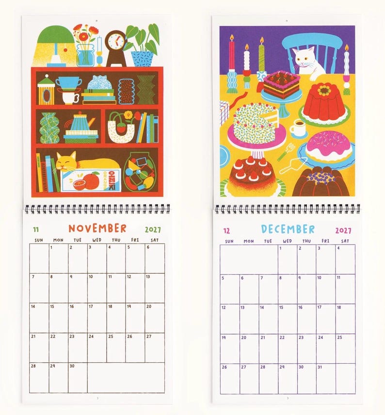 May include: A 2027 wall calendar featuring two open pages for November and December. November displays a red shelf with a cat and various objects. December shows a white cat at a table with cakes and candles. Both pages include a grid calendar.