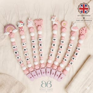May include: Eight pacifier clips featuring silicone beads in shades of pink and white, with charms including a rainbow, cat, unicorn, butterfly, flower, and swan. Each clip includes white letter beads spelling NAME and BABY, attached to light pink clips.