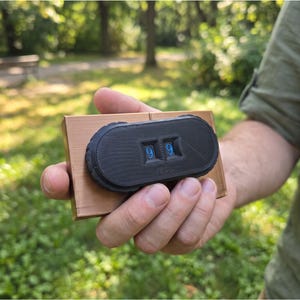 May include: A rectangular copper-colored base supports a black, oval-shaped mechanical counter. The device features two recessed windows displaying the blue numerical digits nine and nine, with a textured surface and a notched outer edge.