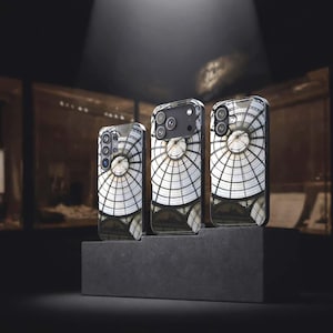 May include: Three smartphone cases featuring a printed design of a glass and metal domed ceiling with a radial grid pattern. The cases are displayed in a row on a dark, tiered platform, showcasing the architectural graphic on the back panels.