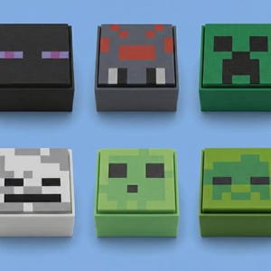 May include: A set of six square, block-shaped containers featuring pixelated character faces. The collection includes black, gray, green, white, light green, and olive green boxes, each topped with a matching lid displaying a unique graphic design.