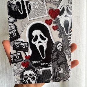 Può includere: Una custodia rettangolare per tablet con un collage in stile ricamo di maschere Ghost Face, cuori rossi, cassette con il testo 'I GAVE YOU MY HEART' ed elementi floreali. Il design include la scritta 'ghost face' in lettere bianche.