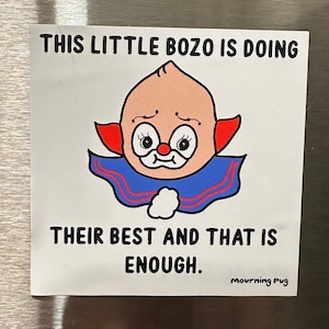 May include: White sticker with a cartoon illustration of a red-nosed clown with a blue and red collar. The text reads "This little bozo is doing their best and that is enough." and "mourning Pug" in the bottom right corner.