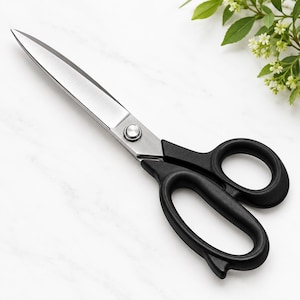 May include: A pair of scissors featuring sharp, silver-toned metal blades and matte black handles. The blades are connected by a central silver screw, and the handles are designed with two distinct finger loops for a secure grip.