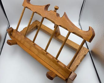 May include: A light brown wooden book stand featuring a rectangular base with a ledge and an adjustable angled support frame. The top rail has a decorative scalloped edge with a small central knob, connected by four vertical wooden dowels.