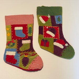 May include: Two patchwork Christmas stockings featuring various holiday-themed fabric appliqués. The left stocking has a red and white chequered cuff, while the right has a green and black chequered cuff. Both display colourful stitched designs.