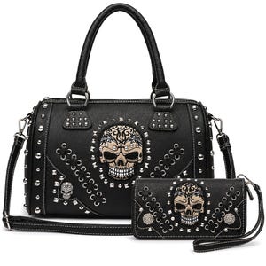 Könnte beinhalten: Eine schwarze Handtasche und ein passendes Portemonnaie mit einer zentralen beigen Totenkopf-Grafik und filigranen Mustern. Beide Artikel sind mit silberfarbenen Nieten, schwarzer Schnürung und weißen Kontrastnähten verziert.