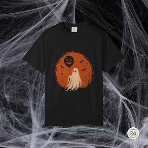 May include: A black short-sleeve t-shirt featuring a graphic print of a white ghost holding a black jack-o'-lantern balloon against a large orange circular background with silhouettes of flying bats and bare tree branches.
