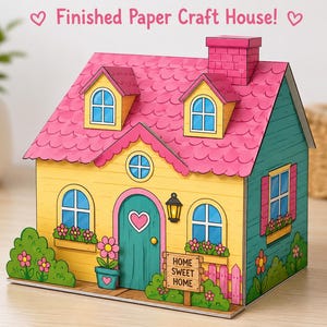 Puede incluir: Una casa de manualidades de papel terminada con fachada amarilla, techo rosa festoneado y puerta color verde azulado con un corazón recortado. La estructura incluye chimenea, buhardillas, jardineras y un letrero que dice "HOME SWEET HOME".