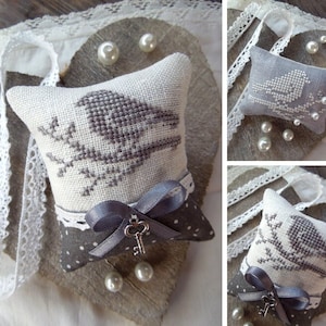 May include: Two gray and white embroidered pillow cushions with a bird design. The pillows are decorated with a gray ribbon and a key charm.