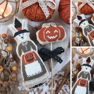 May include: A collection of Halloween-themed handmade crafts. Includes a cross-stitched bunny doll with a pumpkin, a pumpkin-shaped lollipop, and fabric pumpkins with lace bows. The color palette features orange, black, and cream.