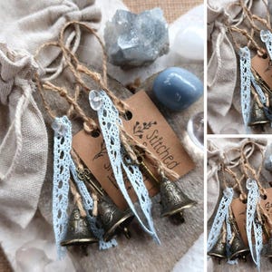 Könnte beinhalten: Ein Set aus vier kleinen, antiken Glocken mit blauer Spitzenborte und einem Schlüsselanhänger. Die Glocken sind mit Schnur zusammengebunden und haben ein braunes Etikett mit der Aufschrift "Stitched & Co."