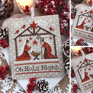 Può includere: Un disegno a punto croce raffigurante una scena della natività con la scritta "Oh Holy Night". L'opera raffigura Maria, Giuseppe e Gesù bambino in una stalla, con stelle e fiocchi di neve. Il disegno è su un tessuto beige con accenti rossi e marroni.