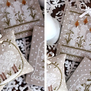 May include: Hand-stitched linen ornaments with festive designs. One features a sheep, another displays candles with the word "Candlemas." The ornaments are beige with white polka dots and are tied with a white ribbon.