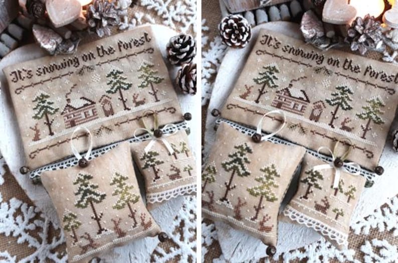 Puede incluir: Un sampler de punto de cruz con el texto "It's snowing on the forest" y una escena de invierno con una caba&ntilde;a, &aacute;rboles y nieve. El sampler est&aacute; enmarcado con un encaje blanco y tiene tres peque&ntilde;os adornos de tela marr&oacute;n con una escena de invierno similar.