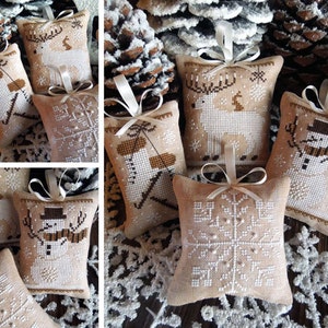 May include: Six handmade Christmas decorations with a winter theme. The decorations are made of burlap fabric and feature embroidered designs of a snowman, a deer, and a snowflake. The decorations are adorned with white ribbon and beads.