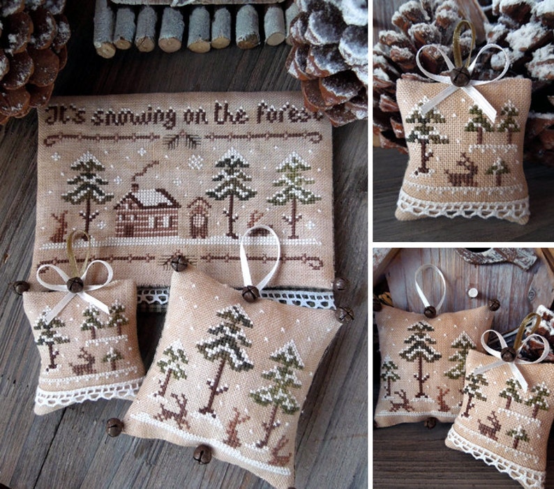 Puede incluir: Tres adornos hechos a mano con punto de cruz con un tema de bosque de invierno. Los adornos son beige con bordados marrones, verdes y blancos. Cada adorno presenta una caba&ntilde;a, &aacute;rboles y ciervos. Los adornos est&aacute;n decorados con un borde de encaje blanco y campanas marrones.