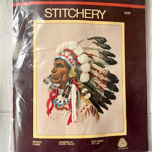 May include: A Sunset Stitchery needlepoint kit titled Indian Chief, designed by Eileen Violet. The package features an embroidered portrait of a person wearing a feathered headdress with white pom-poms, red ribbons, and beads. Fits 16" x 20" frame.