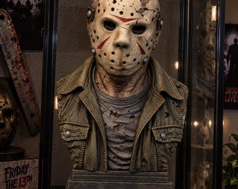 May include: A detailed bust of a hockey mask-wearing figure featuring a weathered, off-white mask with red triangular markings and multiple holes. The figure wears a distressed, olive-green collared jacket over a tattered grey shirt.