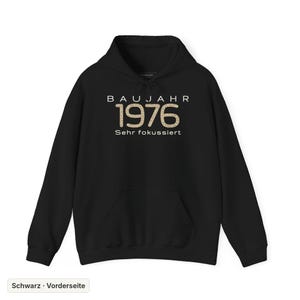 Könnte beinhalten: Ein schwarzer Kapuzenpullover mit dem auf die Brust gedruckten Text BAUJAHR 1976 Sehr fokussiert. Die Zahlen 1976 sind mit einem beigefarbenen und braunen Leopardenmuster gefüllt, während der restliche Text in einer weißen Schrift gehalten ist.