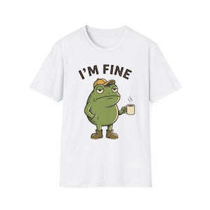 Könnte beinhalten: Ein weißes T-Shirt mit kurzen Ärmeln und einer Grafik eines grünen Frosches, der eine beigefarbene Baseballkappe und braune Stiefel trägt. Der Frosch hält eine dampfende Kaffeetasse und der Text "I'M FINE" steht in schwarzen Buchstaben darüber.
