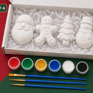 May include: A craft kit containing four white ceramic holiday figures: a Santa Claus, a gingerbread person, a Christmas tree, and a snowman. The set includes six small paint pots in red, green, yellow, blue, white, and black, plus three blue paintbrushes.