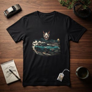 Puede incluir: Una camiseta negra con un estampado gráfico de un coche deportivo color verde azulado derrapando en una carretera sinuosa por la noche, con una máscara de demonio japonesa blanca y roja sobre el coche y humo de neumáticos traseros.