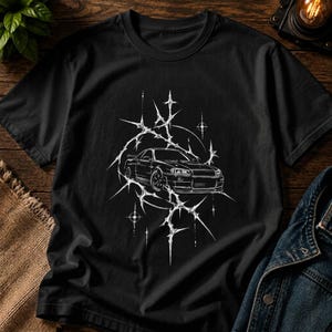 Może przedstawiać: Czarny t-shirt z krótkim rękawem z białym nadrukiem graficznym przedstawiającym samochód sportowy umieszczony w centrum stylizowanego, ostro zakończonego wzoru gwiazdy. Ilustracja ukazuje pojazd z przodu, otoczony cienkimi, poszarpanymi liniami.