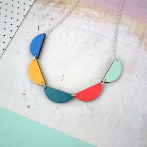 May include: A silver chain necklace with colorful wooden half-circle pendants. The pendants are blue, yellow, teal, red, and green.