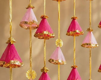 May include: A decorative hanging garland featuring multiple vertical gold ribbons adorned with alternating cone-shaped tassels in shades of hot pink and light pink. Each fabric tassel is finished with a metallic gold trim at the base and top.