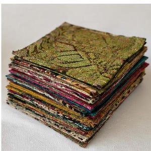 May include: A tall stack of square fabric pieces featuring a variety of intricate patterns and colors. The top piece is primarily green with a dark, detailed botanical print. The layers below display diverse hues including yellow, pink, and teal.