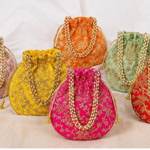Puede incluir: Una colección de seis bolsos redondos con cordón en rosa, amarillo, naranja, verde claro, magenta y rojo. Cada bolso presenta un intrincado bordado floral dorado y un asa hecha de perlas artificiales blancas, con cordones dorados.