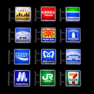 Peut inclure: Une collection de douze enseignes lumineuses carrées présentant divers logos de marques et graphismes de devantures japonaises, dont Asahi, Yakult, FamilyMart, Meiji, Lawson, Pocari Sweat, Tokyo Metro, Osaka Metro, JR East et 7-Eleven, en grille.