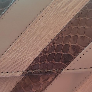 May include: A textured material featuring alternating diagonal panels of smooth beige and brown snakeskin-patterned sections. The panels are joined by visible dark stitching along the edges, creating a geometric pattern with distinct surface textures.