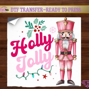 May include: A DTF transfer sheet featuring a pink nutcracker with a white beard, gold accents, and a black belt. The text reads Holly Jolly in pink and light pink script. Includes green holly leaves, red berries, and a string of colourful lights.