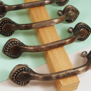 May include: Four antique-style cabinet knobs with a distressed bronze finish. Each knob features a decorative, beaded, heart-shaped design.
