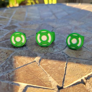 May include: Three rings featuring a bright green circular frame with a white center disc. Each ring displays a raised green lantern symbol design on the face, characterized by a central circle enclosed within a stylized geometric border.