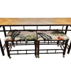 May include: A rectangular console table with a light wood veneer top and a dark brown bamboo-style frame. Two matching stools with dark brown bamboo-style frames and cushions featuring a tropical leaf and hibiscus flower print.