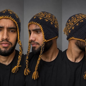 May include: A dark navy blue and mustard yellow knit hat featuring a geometric pattern, ear flaps, and braided tassels. The hat is shown from three different angles, displaying the intricate yarn work and the braided ties hanging down.