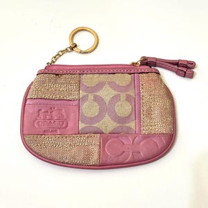 Könnte beinhalten: Eine rosa und beige Coach-Geldbörse mit einem Patchwork-Design aus Leder- und strukturierten Stoffeinsätzen. Das Accessoire verfügt über einen goldfarbenen Metallschlüsselring an einer Kette, einen Reißverschluss mit Lederanhänger und ein Logo.