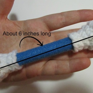 May include: A blue and white crocheted toy bone, about 6 inches long. The bone is made of a blue foam tube covered in white crocheted fabric.
