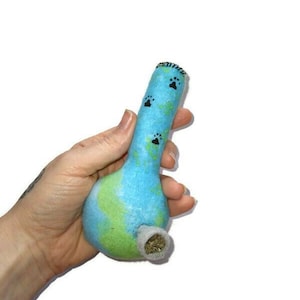 Puede incluir: Una pipa de fieltro azul y verde con diseños de huellas de patas. La pipa está llena de hierbas secas.