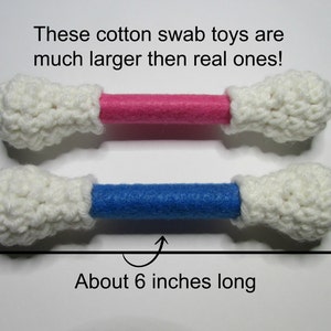May include: Two crocheted cotton swab toys, one with a pink and one with a blue center, are about 6 inches long. These are much larger than real cotton swabs.