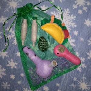 May include: A green mesh bag filled with various felt toys, including a taco, a green bud, two white joints, and two purple and pink pipes.