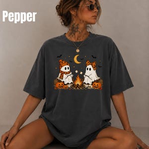 Op de afbeelding: Een antracietgrijs t-shirt met korte mouwen en een afbeelding van twee geesten die marshmallows roosteren boven een kampvuur. De geesten dragen oranje mutsen en sjaals met patronen. Het ontwerp bevat pompoenen, een maansikkel en vleermuizen. De tekst Pepper is zichtbaar.