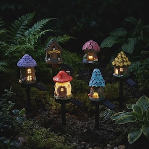 May include: Six miniature garden stake lights shaped like small houses and mushrooms, each featuring a unique roof design in purple, brown, pink, red, blue, or yellow, with warm glowing windows and solar panels attached to black stakes.