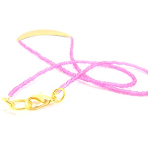 May include: A pink beaded necklace with a gold clasp. The necklace is made of small, round beads and has a simple, elegant design.